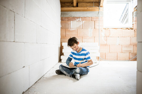 Smiling boy writing in book while sitting at attic during rebuilding