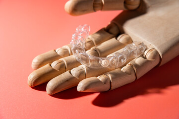 Close-up of wooden elegant hand holding invisible clear aligners, on pastel pink background. Healthy lifestyle and teeth concept