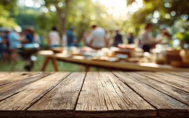 Wooden table surface with blurred outdoor barbecue party background and people gathering. Empty deck space for product display against social dining setting