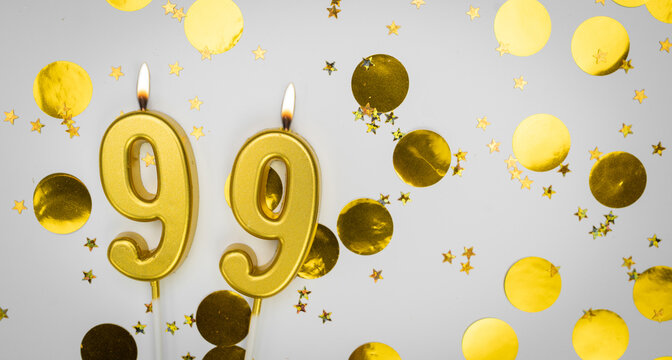 Number 99 golden celebration birthday candle on white with confetti background. Ninety-nine years birthday. Concept of celebrating birthday, anniversary.