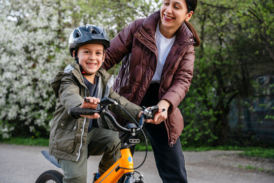 Mother teaching son to ride a bicycle outdoors in a fun and supportive environment
