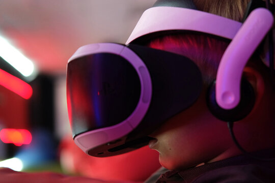 Fototapeta Child wearing VR Glasses. Surprised kid boy having fun play VR headset, virtual reality goggle, 3D cyber space. Futuristic neon blue red UV lighting. Digital technology, metaverse game, entertainment