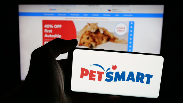 Stuttgart, Germany - 05-25-2025: Person holding mobile phone with logo of US pet retail company PetSmart Inc. on screen in front of web page. Focus on phone display.