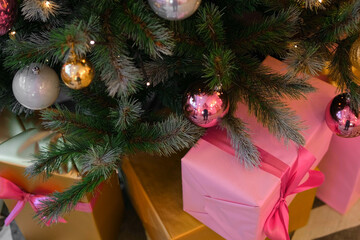 Big Wrapped Gift Boxes Is Under the Christmas Tree. Pink and Gold Gift-Wrapped Box with Ribbon for Friends, Relatives. Close up. Packaging of Xmas Presents. Festive Decorations. Preparing for Holidays