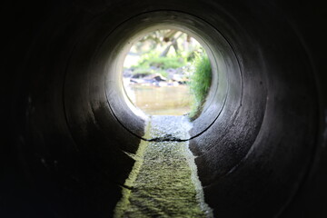 View through a round concrete tunnel carrying a stream beneath a road