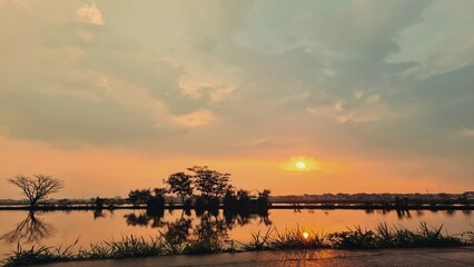 Sunset over calm water reflecting the sky and trees
