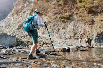 Hiker with backpack walking through mountain stream. Woman hiking in nature.
