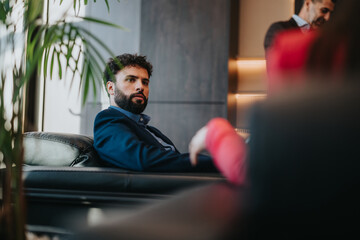 A professional man sits attentively in a stylish office environment, surrounded by colleagues,...