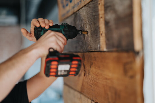 Hands operating a cordless electric drill to fix screws into wooden boards, showcasing skilled craftsmanship, home improvement, and woodworking concepts in a detailed image.