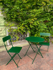 green chairs and a table against a wall wrapped in wisteria