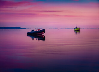 Pink summer sunrise on Baltic sea with two boats. Calm morning seascape of Baltic sea. Wonderful outdoor scene of Rewa public beach, Poland, Europe. Beauty of nature concept background.