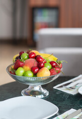 Colorful fresh fruit bowl on hotel room counter with armchair, bed and lampshade showing in the background