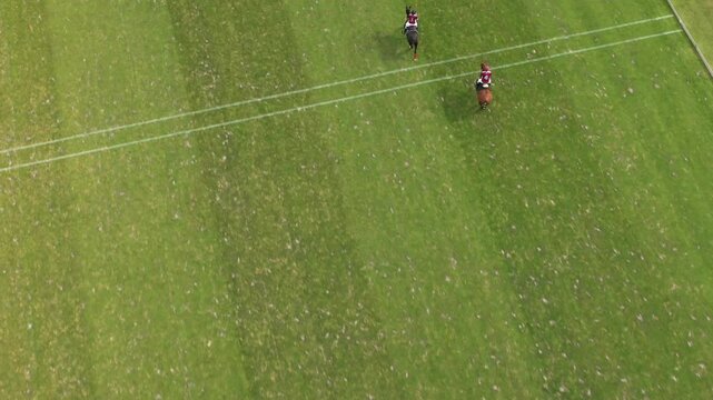 High angle aerial drone shot captures polo players on horseback competing across a vast, striped green field at prestigious Chantilly Polo Club, France