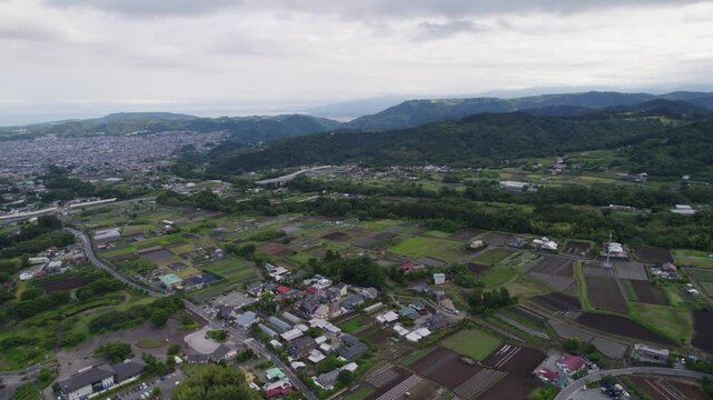Drone footage of Hadano&rsquo;s rural landscape with neatly arranged farmland, village homes, and green hills under cloudy skies. A peaceful and scenic countryside view in Japan.