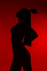 Silhouette of a woman sport fitness posing with a raised arm against a striking red background, highlighting athletic form and strength in dynamic shadow play.