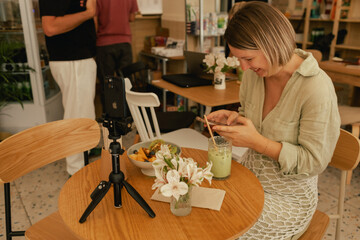 Middle-aged woman is video blogging in a cafe on a phone with a tripod. Small business. Using phone...