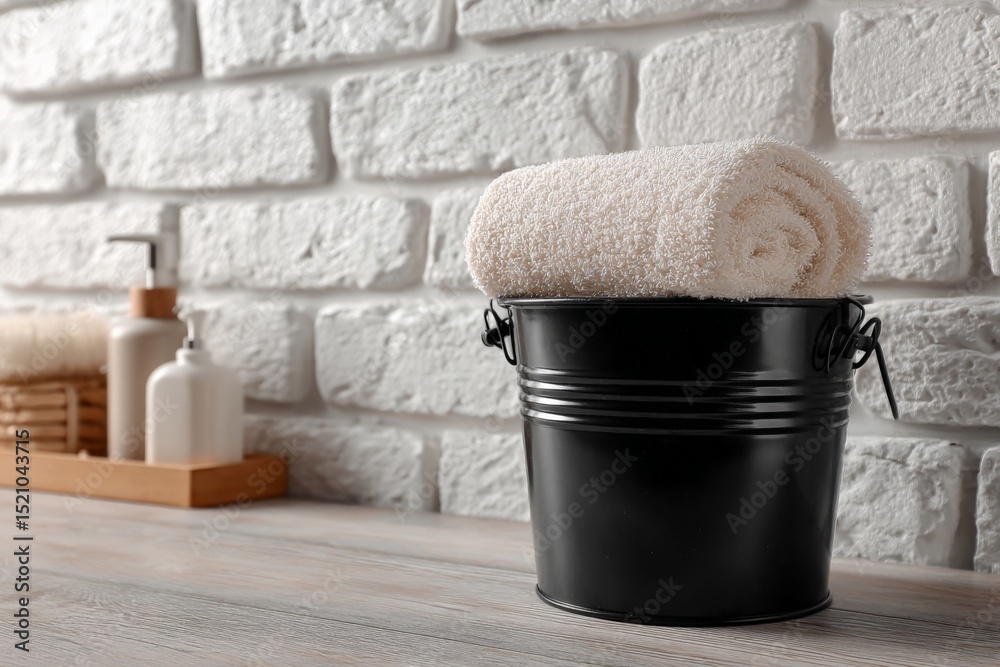 Poster relaxing spa setting with rolled towel in black bucket against textured brick wall