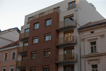 The image shows a modern apartment building facade with a mix of materials and balconies, located in an urban setting, reflecting contemporary architecture and current housing trends
