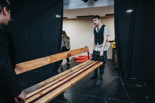 Actors set up and carry props behind the curtain in preparation for a theatrical production, showcasing teamwork, effort, and creative dedication.