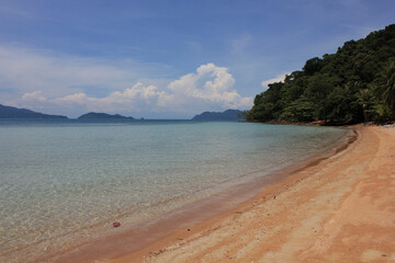 Curved Beach and Calm Sea Horizon. A wide-angle view of a quiet sandy beach curving gently toward the clear horizon, framed by green hills and tropical sea.