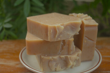 Handmade Tamarind Oatmeal Soap Bars. A stack of handmade tamarind and oatmeal soap bars placed on a white dish, photographed outdoors in natural lighting with a green garden background. 