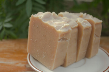 Handmade Tamarind Oatmeal Soap Bars. A stack of handmade tamarind and oatmeal soap bars placed on a white dish, photographed outdoors in natural lighting with a green garden background. 