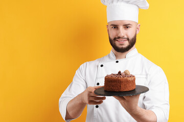 Happy confectioner in uniform holding chocolate cake on orange background