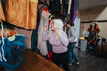 A creative environment showing young people trying on costumes, surrounded by colorful clothing and...