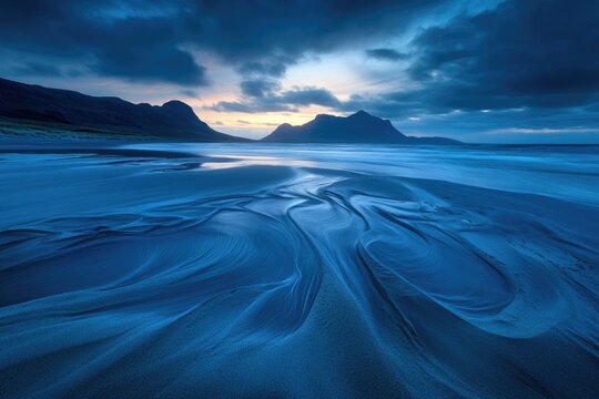 Serene twilight scene at the beach with mountains in background. Blue hour casts a magical glow on the sand patterns.