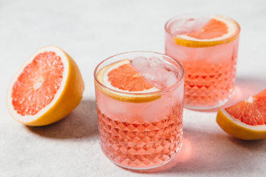A refreshing negroni rosa cocktail served in a textured glass with ice, garnished with a slice of pink grapefruit, set against a light background. Summer party drink recipe, beverages menu.