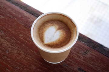 Coffee latte art milk foam on cup on wood background
