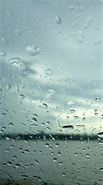 Raindrops on glass. In the background is a blurred image of the sea surface. Shot from the shore