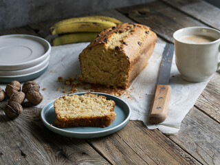 slice of banana bread on a plate accompanied by coffee, nuts, fresh fruit, on a rustic wooden table. Artisanal breakfast, slow and conscious living