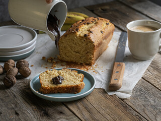 Ceramic jug serving chocolate on a slice of homemade banana bread, accompanied by coffee, fruit and nuts. Slow and conscious living, artisanal breakfast.