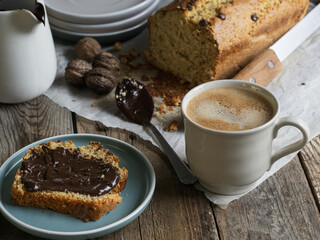 Artisanal and slow breakfast on a wooden table with natural side light. Banana bread with chocolate, impregnated peas, cup of coffee, fresh fruit and nuts. Natural and welcoming layout