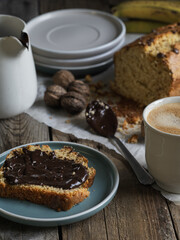 Artisanal and slow breakfast on a wooden table with natural side light. Banana bread with chocolate, impregnated peas, cup of coffee, fresh fruit and nuts. Natural and welcoming layout