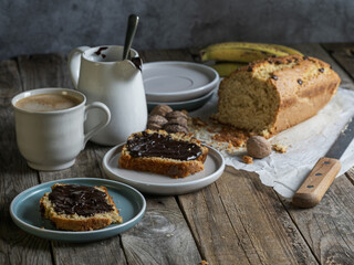 Artisanal and slow breakfast for two. Slices of banana bread with chocolate, coffee, fruit and nuts. Cozy, rustic and natural atmosphere with side light