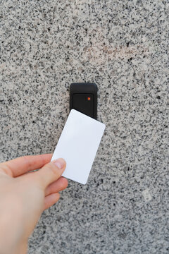 Close-up of a female hand holding a keychain with a key fob near a key reader access device on a building&rsquo;s exterior wall with door. modern security, smart access, and contactless entry technology