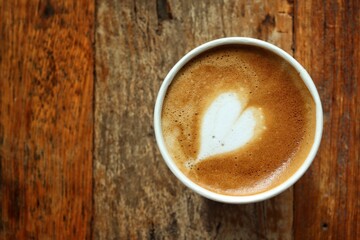 Coffee latte art milk foam on cup on wood background