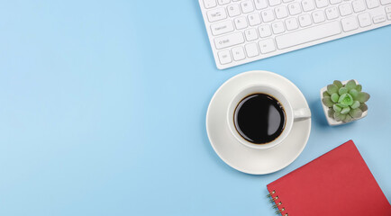 flat lay of red  diary or planner with computer keyboard, black coffee cup and succulent plant pot on blue blackground with copy space.