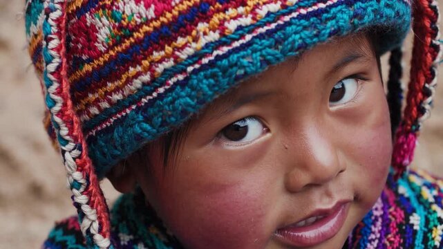 Close up of a young Peruvian child with rosy cheeks, wearing a colorful Andean hat and sweater, looking curiously at something off camera