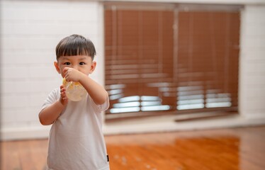 Young child enjoys drink in bright indoor space with wooden floor and natural light during daytime