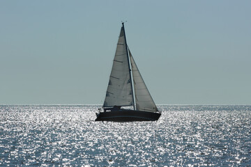 The outline of a sailboat on the sea and bright glare of sunlight on the water. Evening and thick...