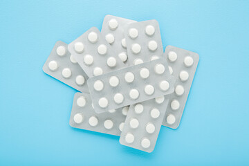 New blister packs of white pills on light blue table background. Pastel color. Closeup. Top down view.