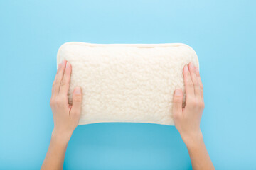 Young adult woman hands touching new clean white soft natural sheep wool pillow on light blue table background. Pastel color. Closeup. Point of view shot. Top down view.