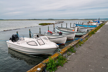 Several small boats are secured at a dock along a peaceful waterway, surrounded by flat waters and gentle clouds above.