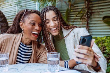 Two multi ethnic women are sharing a funny moment, laughing while looking at a smartphone during a...