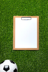 Obraz premium A soccer ball and clipboard with white paper sheet on a green field.