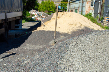 Gravel and sand are piled at a construction site with a truck parked nearby under clear blue skies...