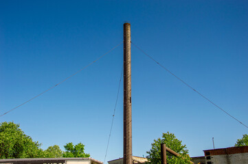 A tall wooden utility pole supports overhead cables under a bright blue sky while surrounded by...